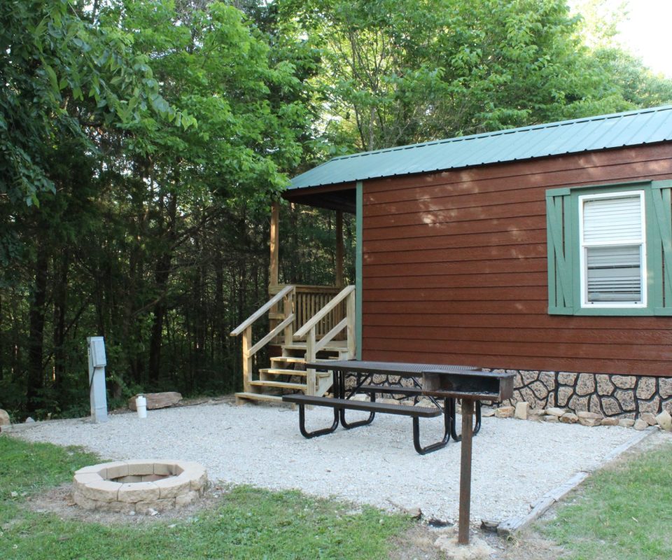 exterior view of cabin with fireplace and picnic table at Great Escapes RV Resorts Branson