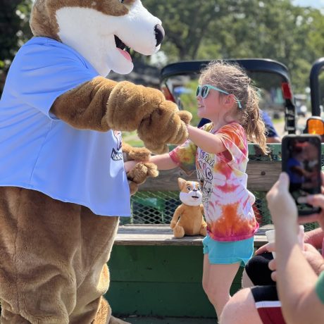 Biscuit the dog mascot at Great Escapes RV Resorts Branson dancing with a little girl camper on wagon ride | amenity at Great Escapes RV Resorts Branson MO
