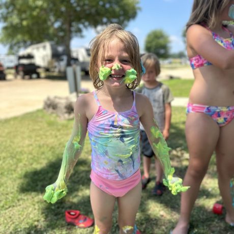 smiling girl in a bathing suit with green foam all over her arms and face | a planned event at Great Escapes RV Resorts Branson